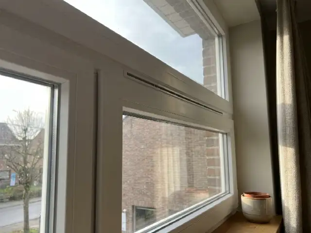 Ventilatierooster bovenaan een raam in een woonkamer